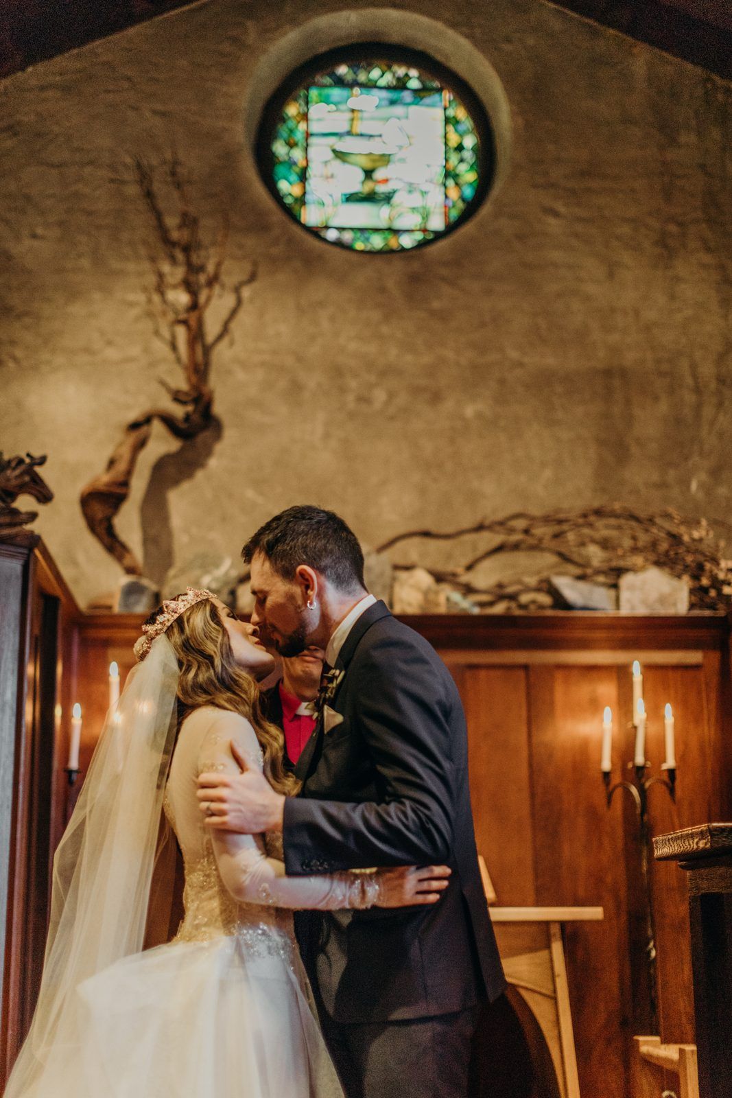 The couple kiss in front of the church's round stained glass window, the bride's veil falling behind her.