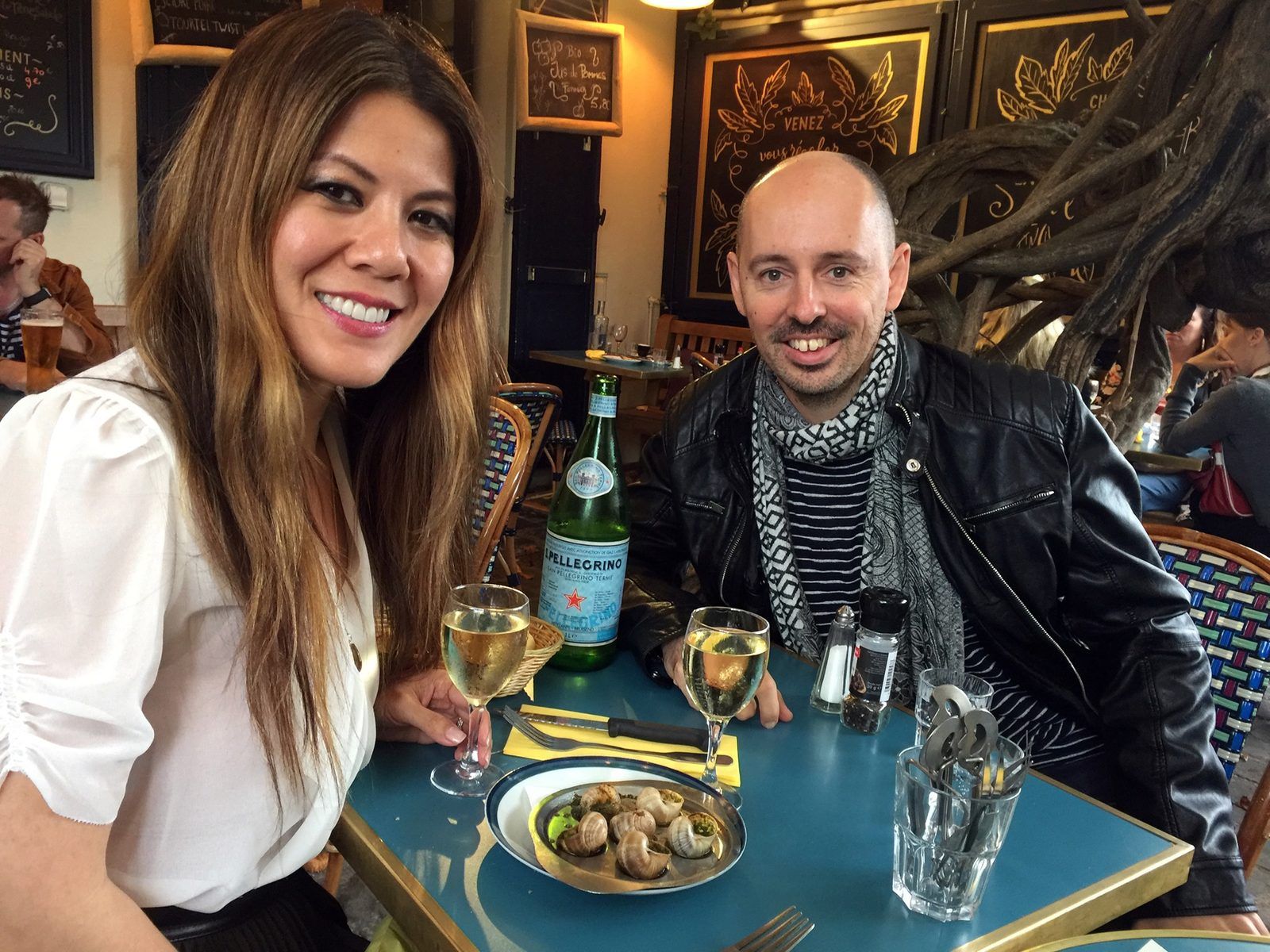 Rena and her pen pal smiling at a cafe table in Paris, a plate of snails and two glasses of white wine in front of them.