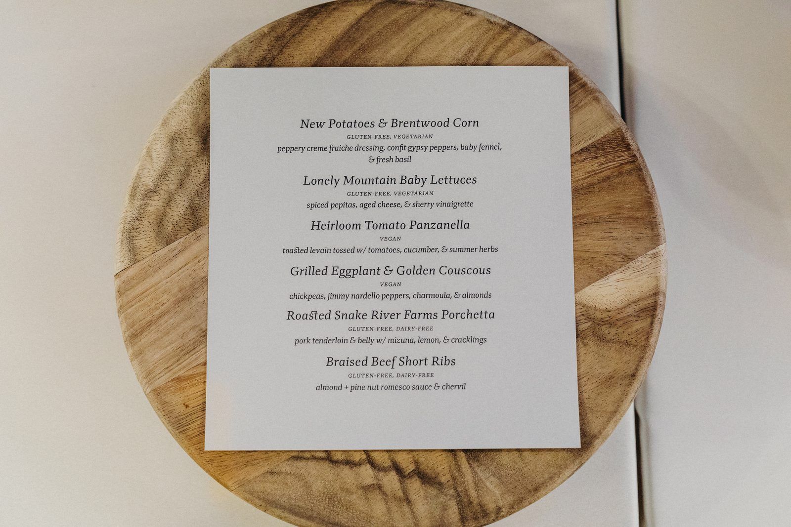 The printed dinner menu on the day: a plain white card laid on a round wooden board on a white tablecloth.